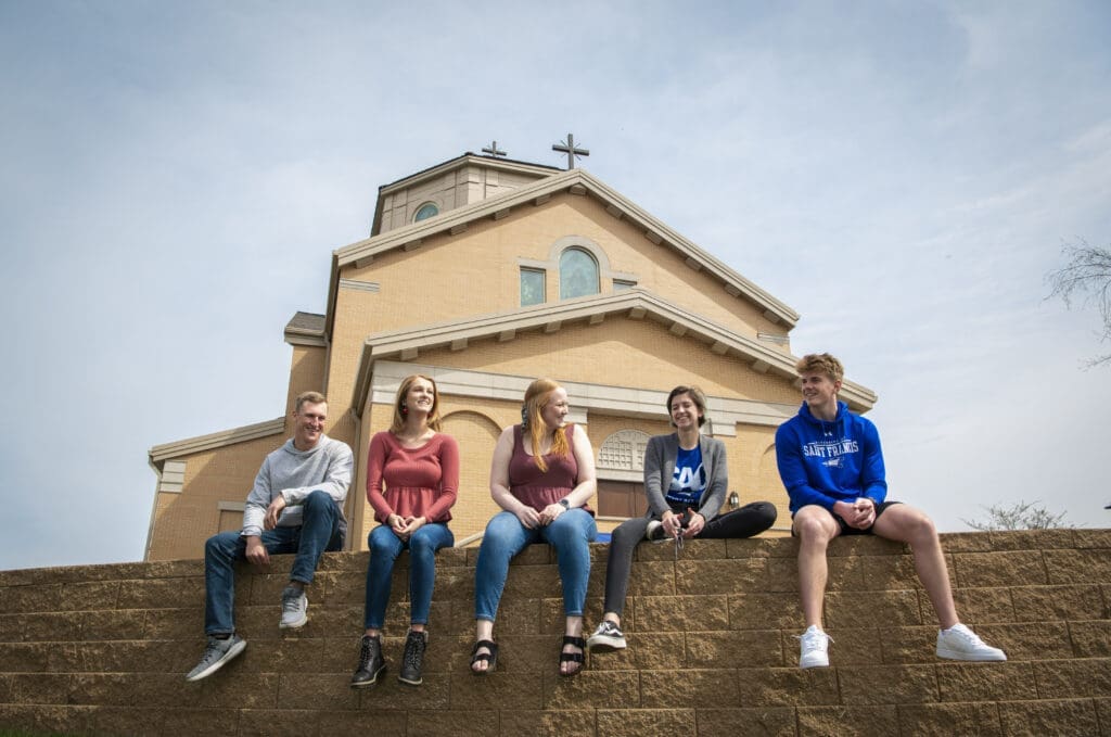 Students sitting on a wall ledge in front of the chapel.