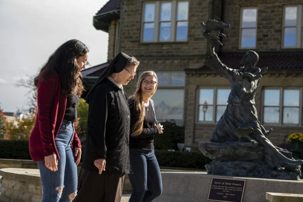 Students walking with a sister. Saint Francis statue in the background.