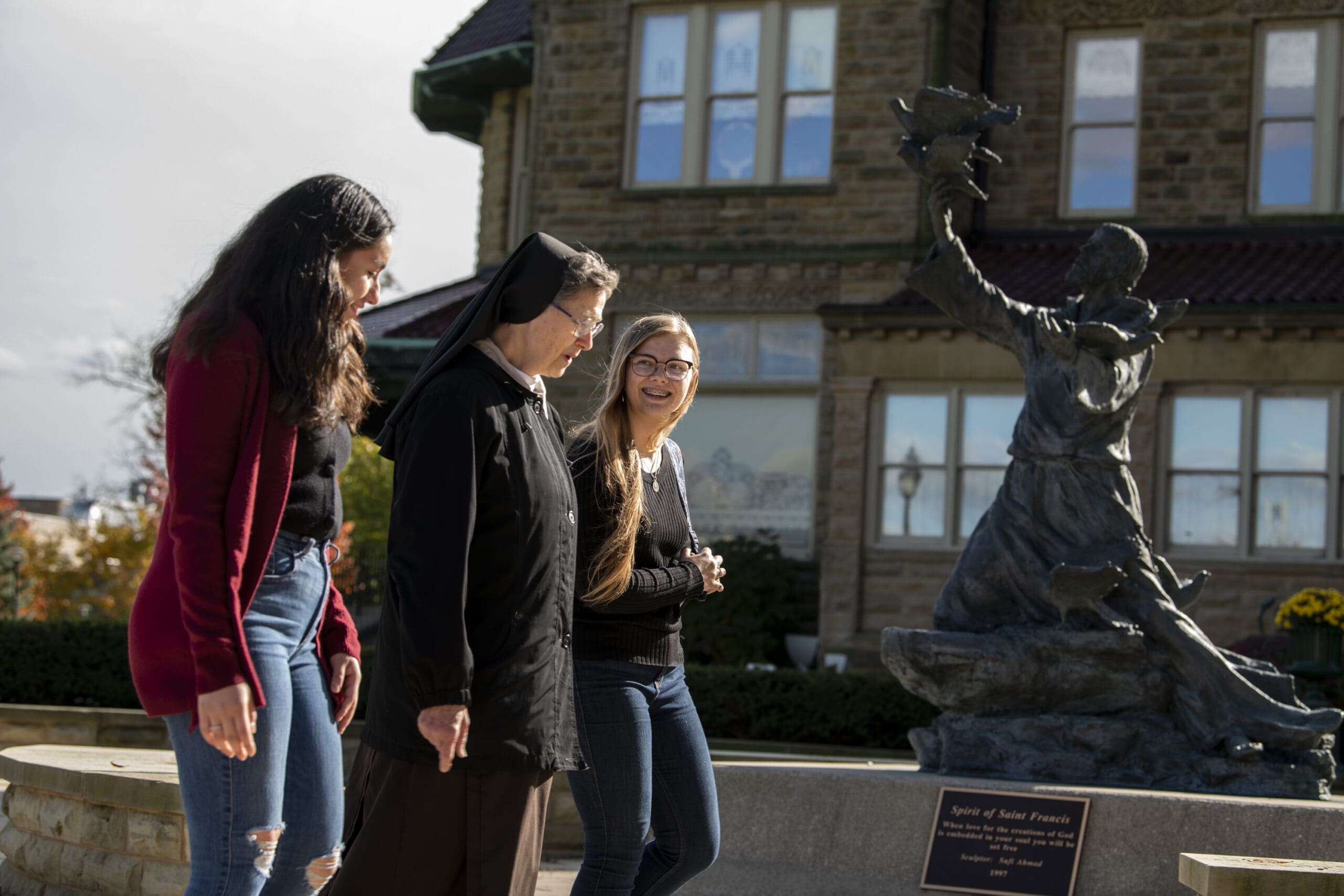 Sister walking with students near Saint Francis Statue.