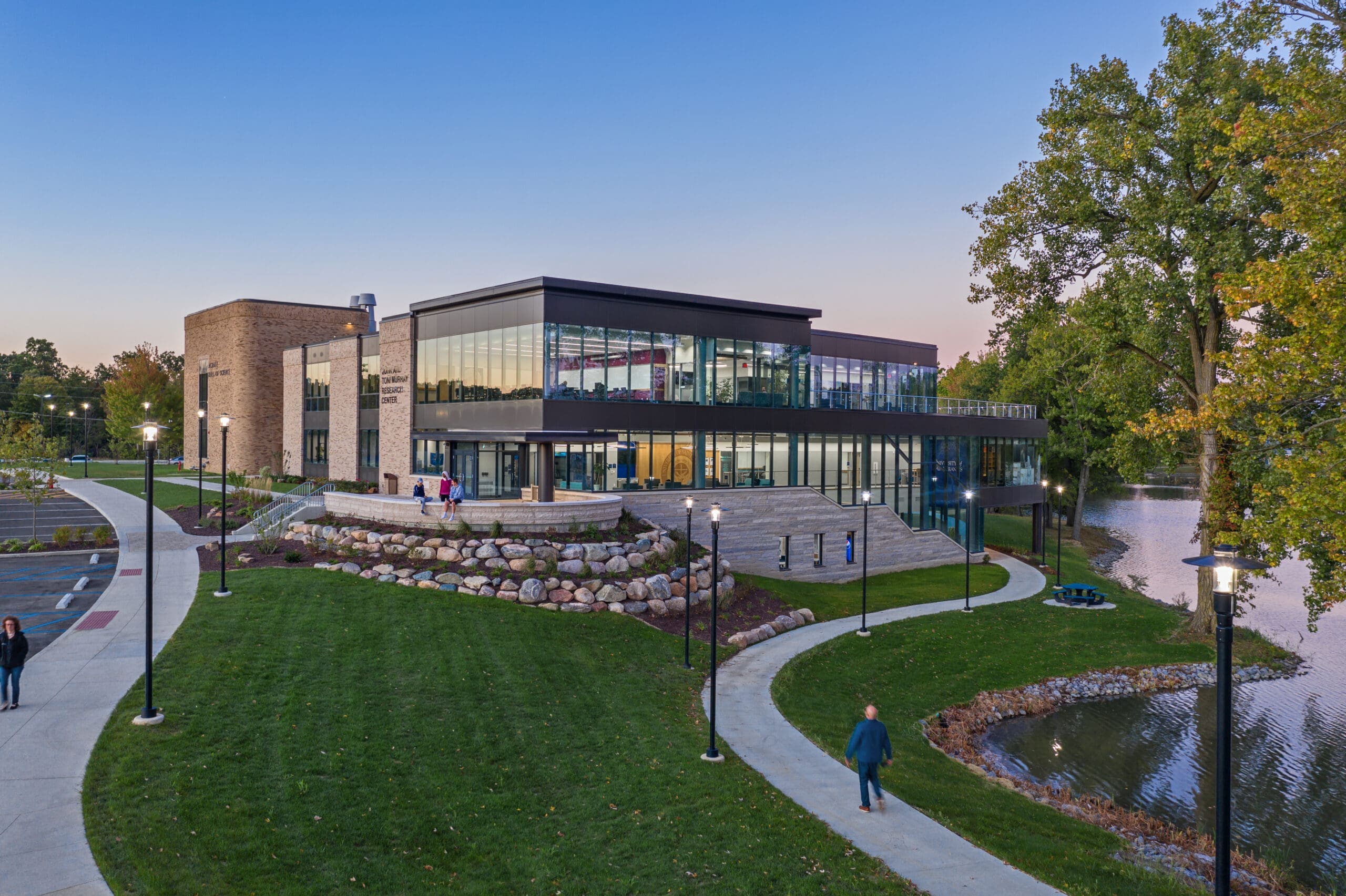 3 people sit on the overlook outside of the Achatz Hall of Science and the John and Toni Murray Research Center while two other people walk down pathways