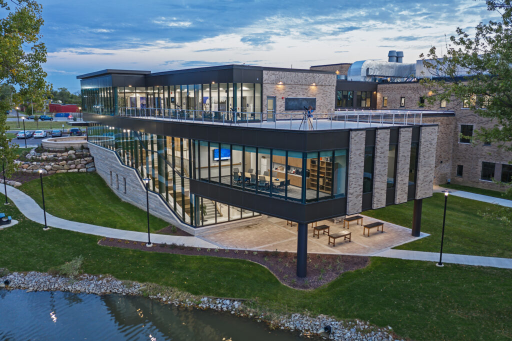 The John and Toni Murray Research Center lit up on a summer evening with a woman using the telescope to view the evening sky