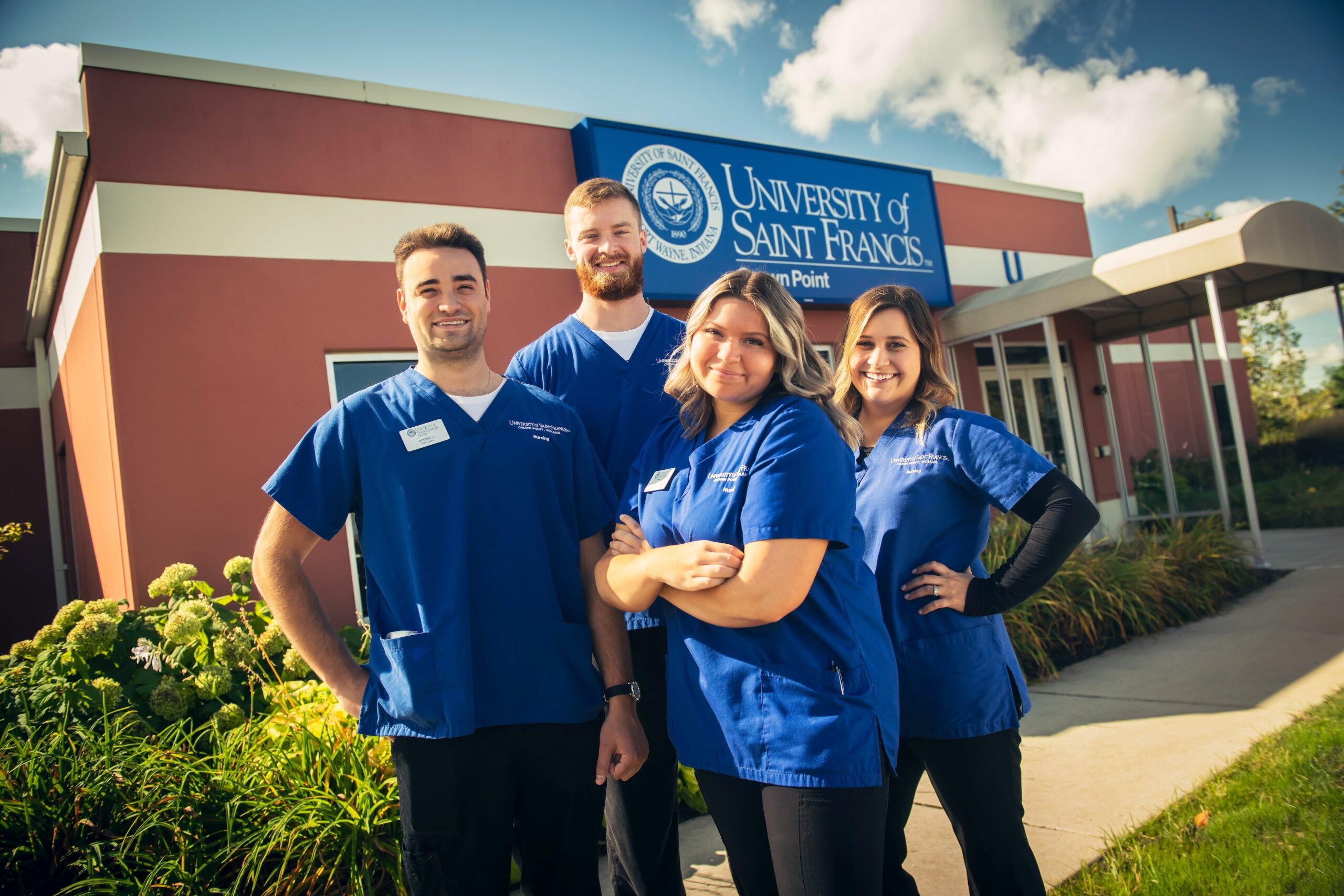 Four students in medical scrubs pose outside the University of Saint Francis Crown Point building.