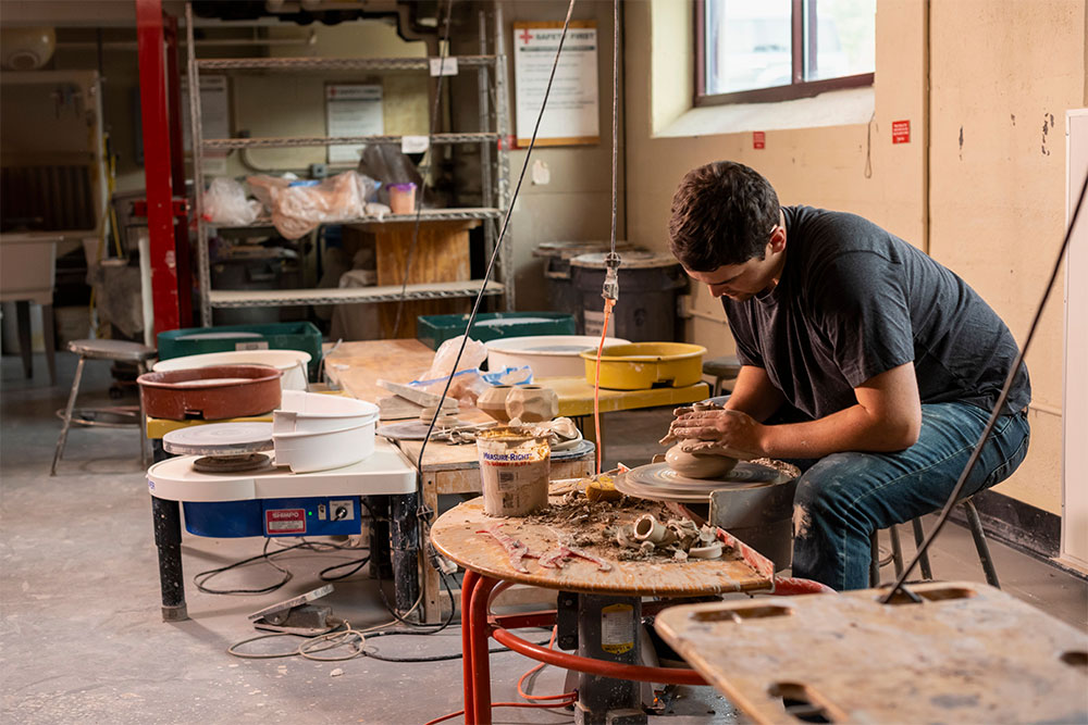 A lone student throws pottery on the ceramics wheel in the ceramics studio